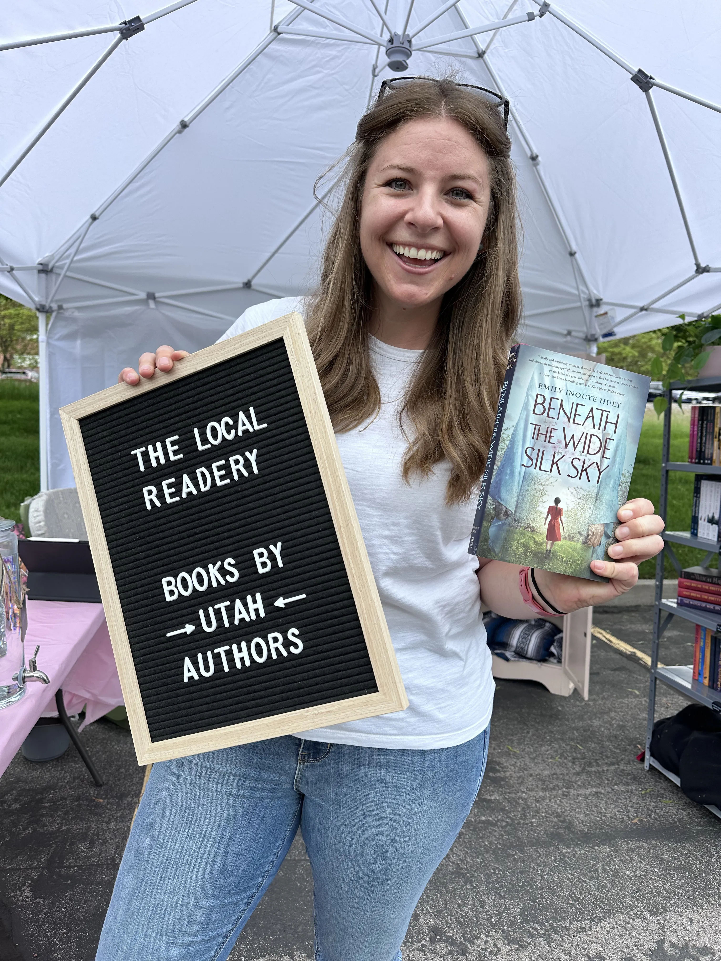 Quaelii holding a letter board and a Utah author book at the pop-up tent